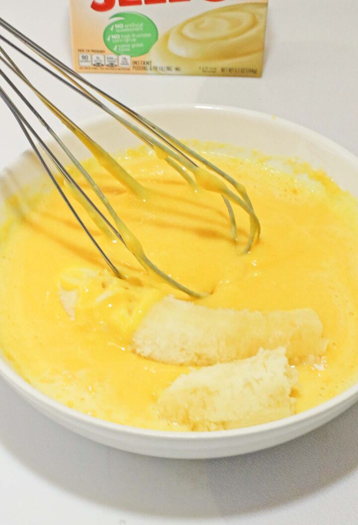 Bowl with sliced bananas and yellow pudding mix being whisked together for a delicious banana cream poke cake recipe—no egg required.