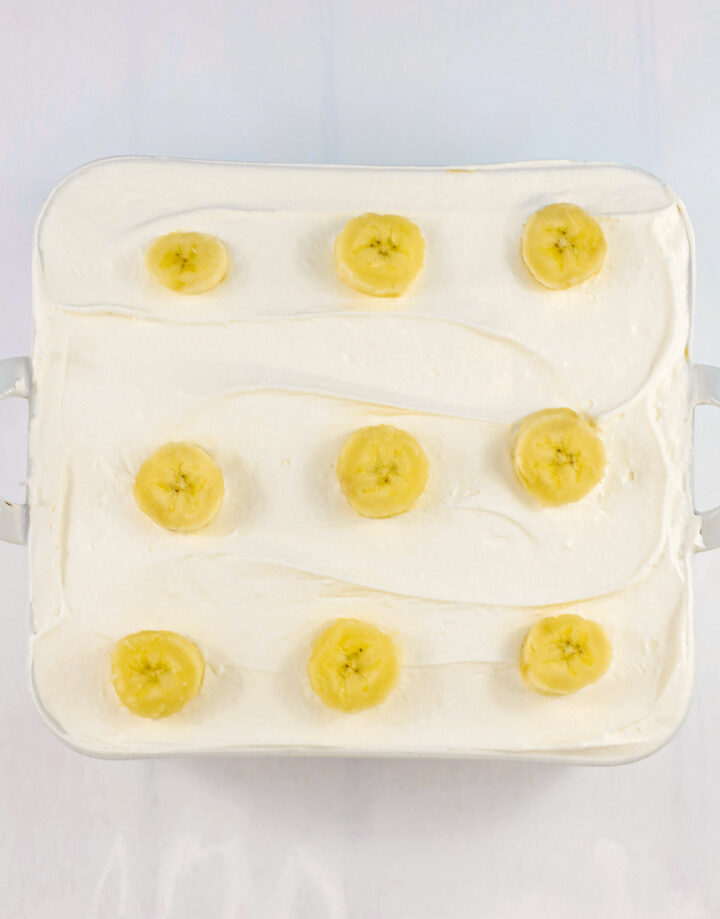 Rectangular Banana Cream dessert topped with smooth white cream and nine banana slices arranged in rows; a delicious no egg treat.