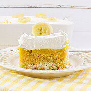A slice of banana pudding poke cake with whipped topping and a banana slice on a white plate—made with creamy banana cream and no egg for a light, irresistible treat.