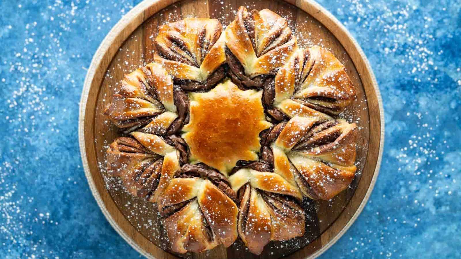 A star-shaped chocolate bread on a wooden platter, dusted with powdered sugar, on a blue background.