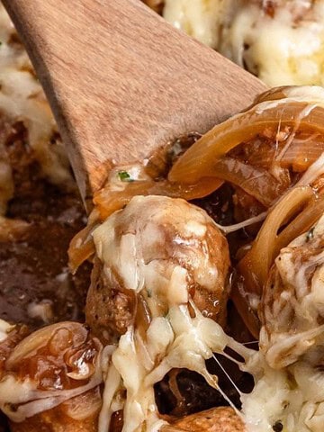 Cheesy meatballs with caramelized onions, garnished with herbs and served with melted cheese on top—perfect for fans of comforting slow cooker recipes.