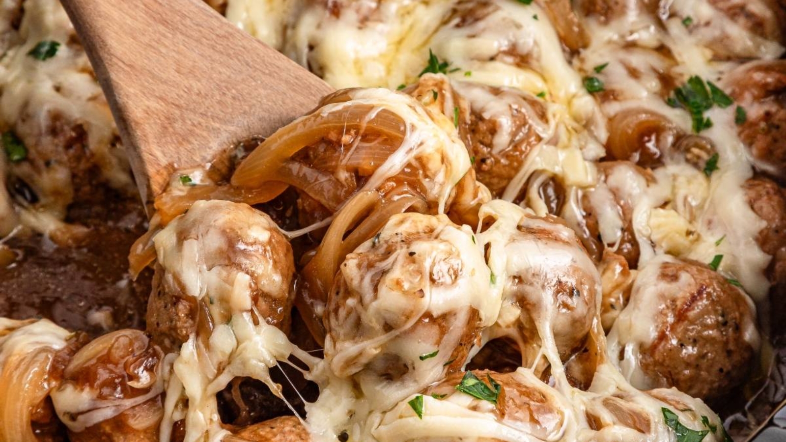 Cheesy meatballs with caramelized onions, garnished with herbs and served with melted cheese on top—perfect for fans of comforting slow cooker recipes.