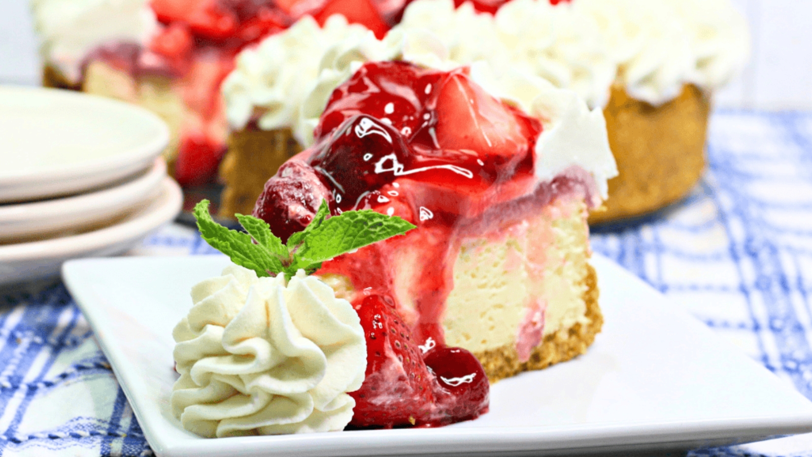 A slice of cheesecake topped with strawberry sauce, whipped cream, and a mint leaf on a white plate&mdash;perfect for celebrating with Mother's Day desserts.