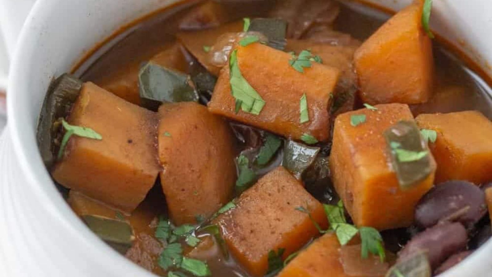 Bowl of stew with chunks of sweet potato, green peppers, beans, and garnished with fresh herbs.