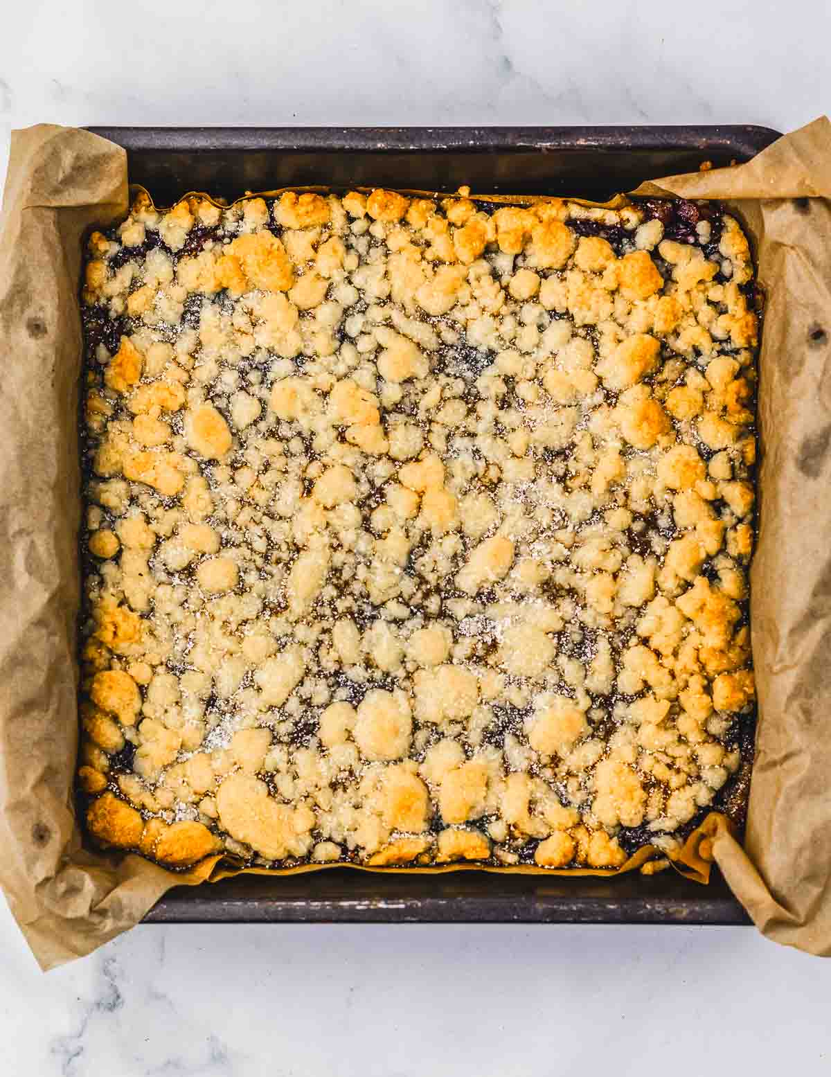 A square pan lined with parchment paper holds golden, crumbly cherry pie crumb bars&mdash;an irresistible dessert recipe.