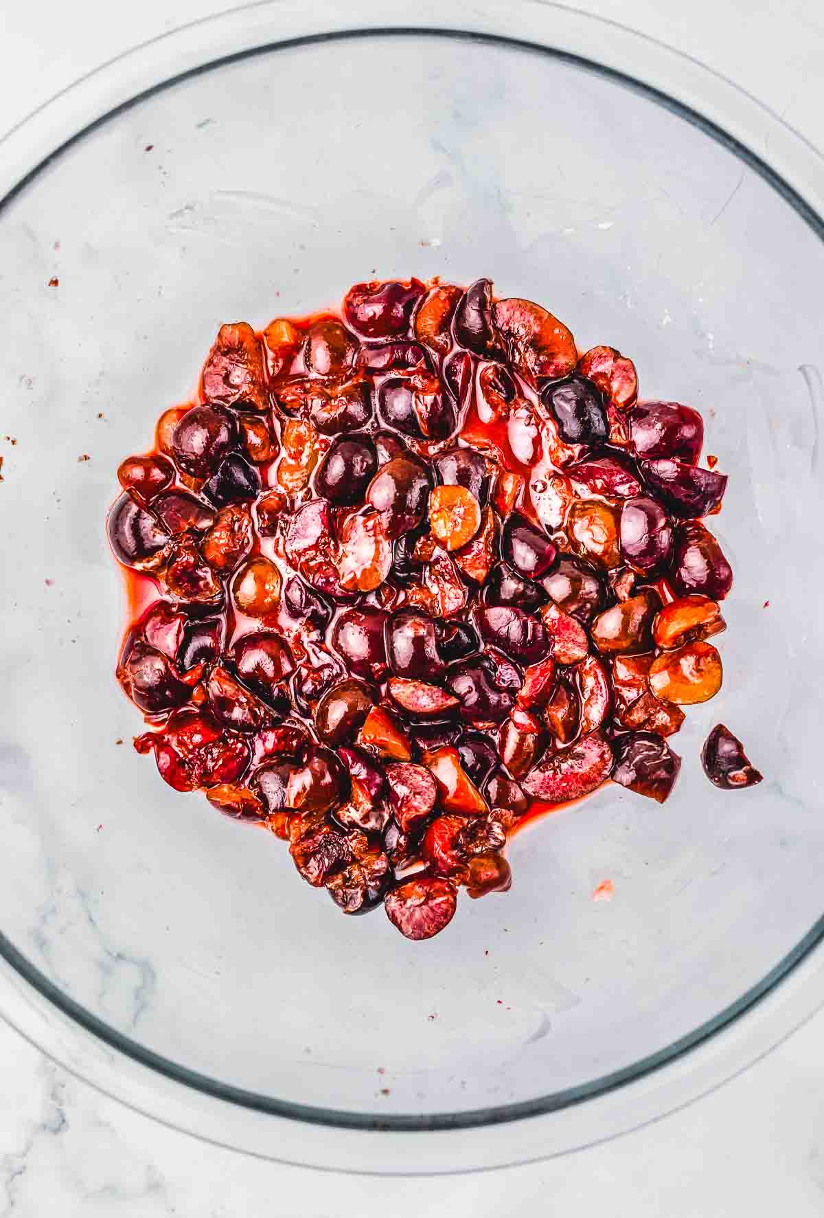 Chopped cherries with juice in a clear glass bowl on a white surface&mdash;perfect for your next Cherry Pie or Crumb Bars recipe.