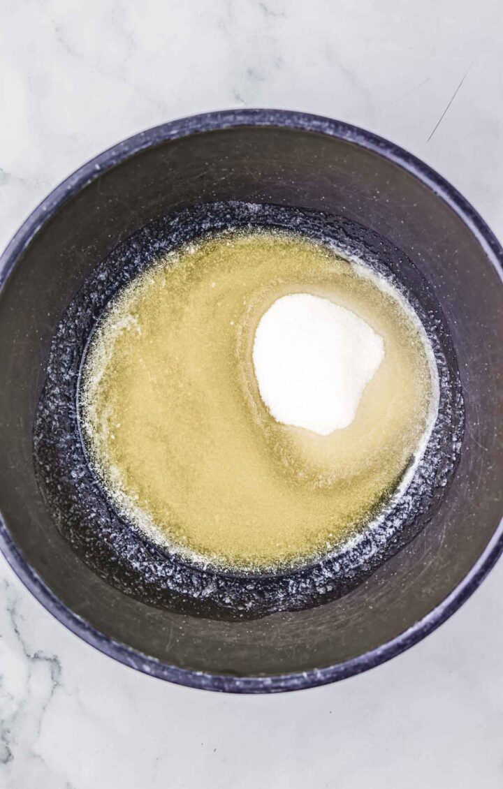 A black bowl with sugar and gelatin powder on a white marble surface, perfect for your next cherry pie recipe.