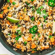 A delicious Rice Skillet filled with cheesy rice, black beans, sweet potatoes, jalapeño slices, lime wedges, and fresh herbs.