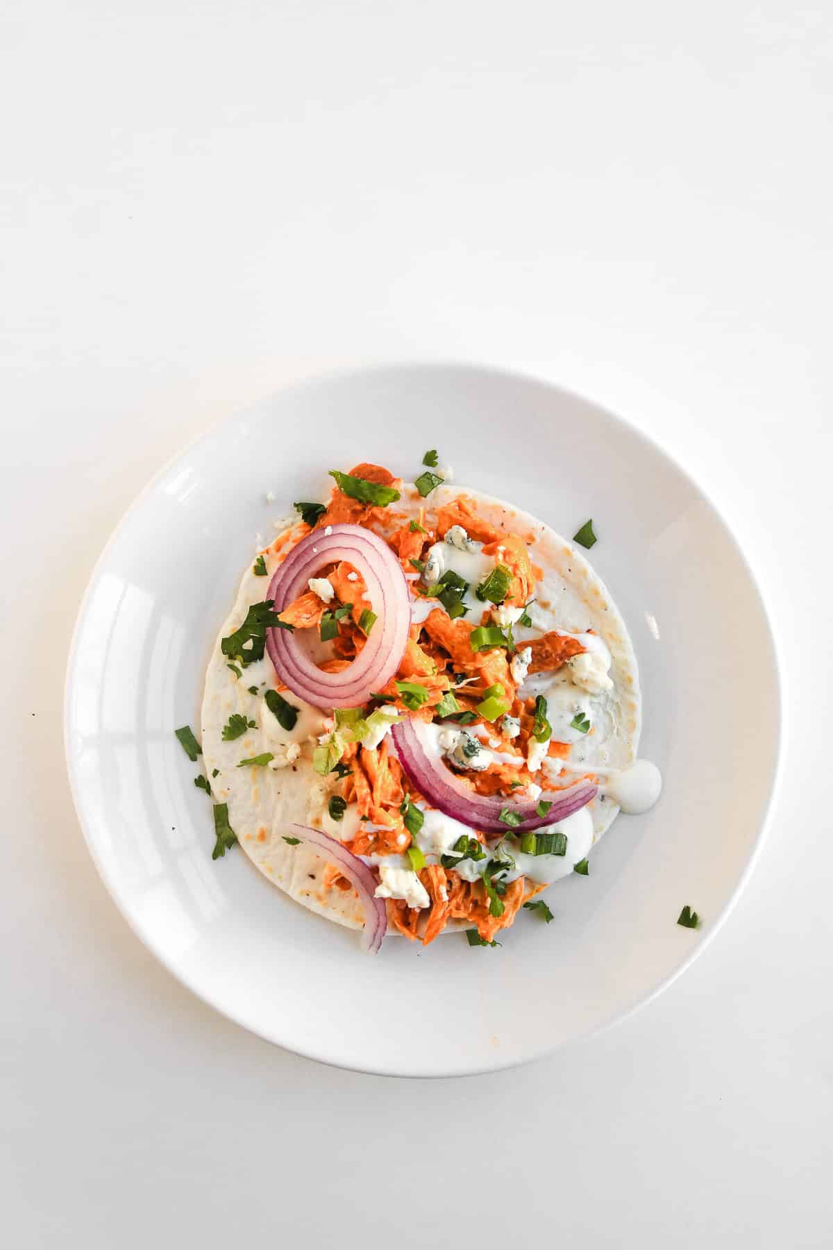 Easy Chicken Tacos with red onions, cilantro, and sauce on a white plate, set against a white background.