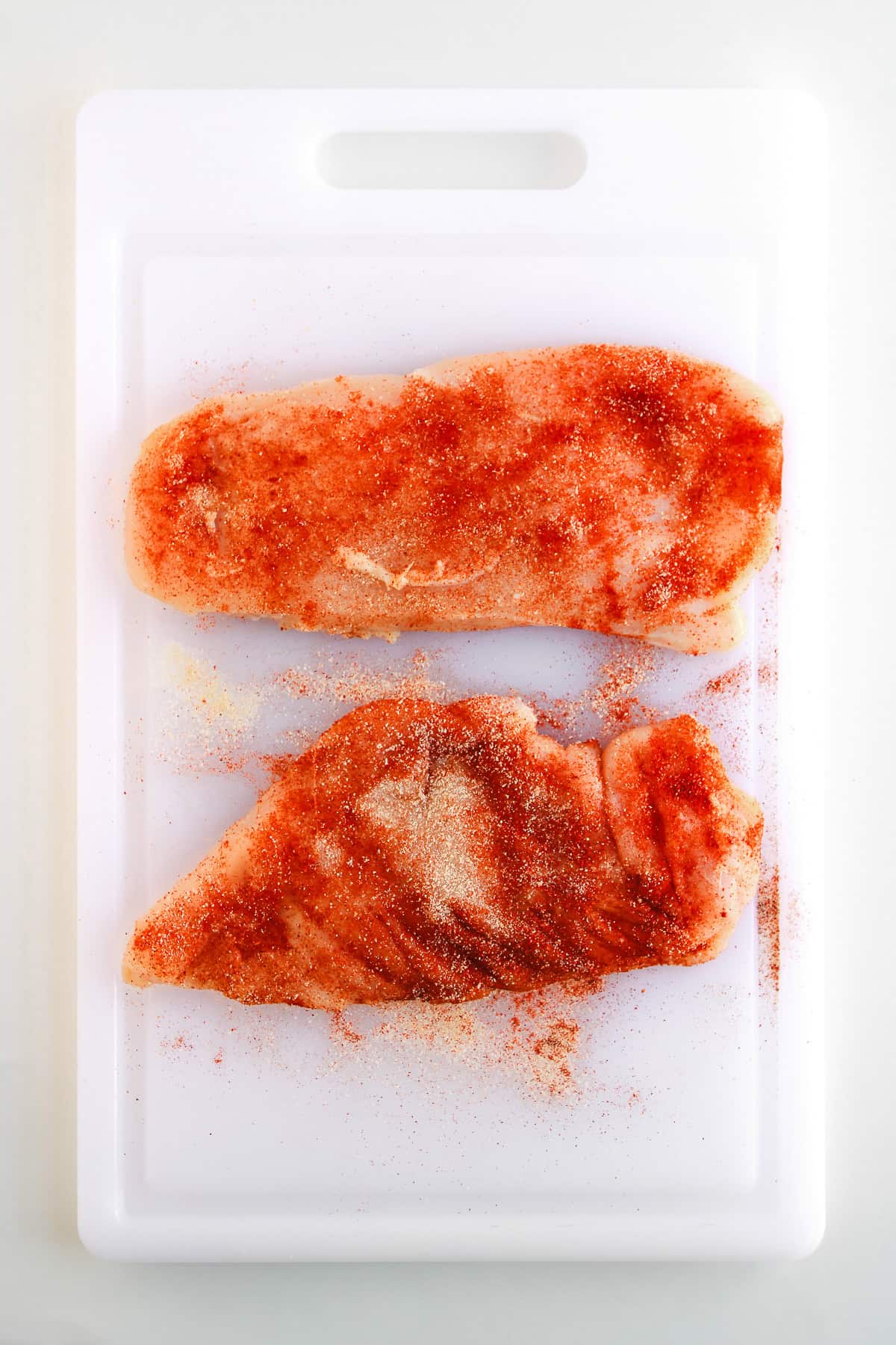 Two raw chicken breasts coated with spicy Buffalo Chicken seasoning rest on a white cutting board, ready to be transformed into flavorful Easy Tacos.