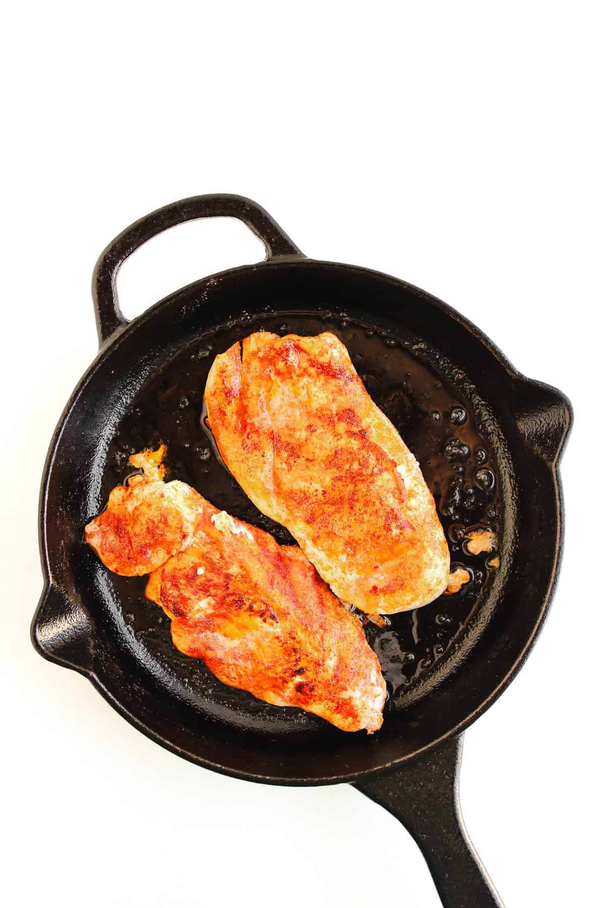 Two cooked, seasoned chicken breasts in a black cast iron skillet on a white background—perfect for making Buffalo Chicken Tacos or adding bold flavor to your next batch of Easy Chicken Tacos.