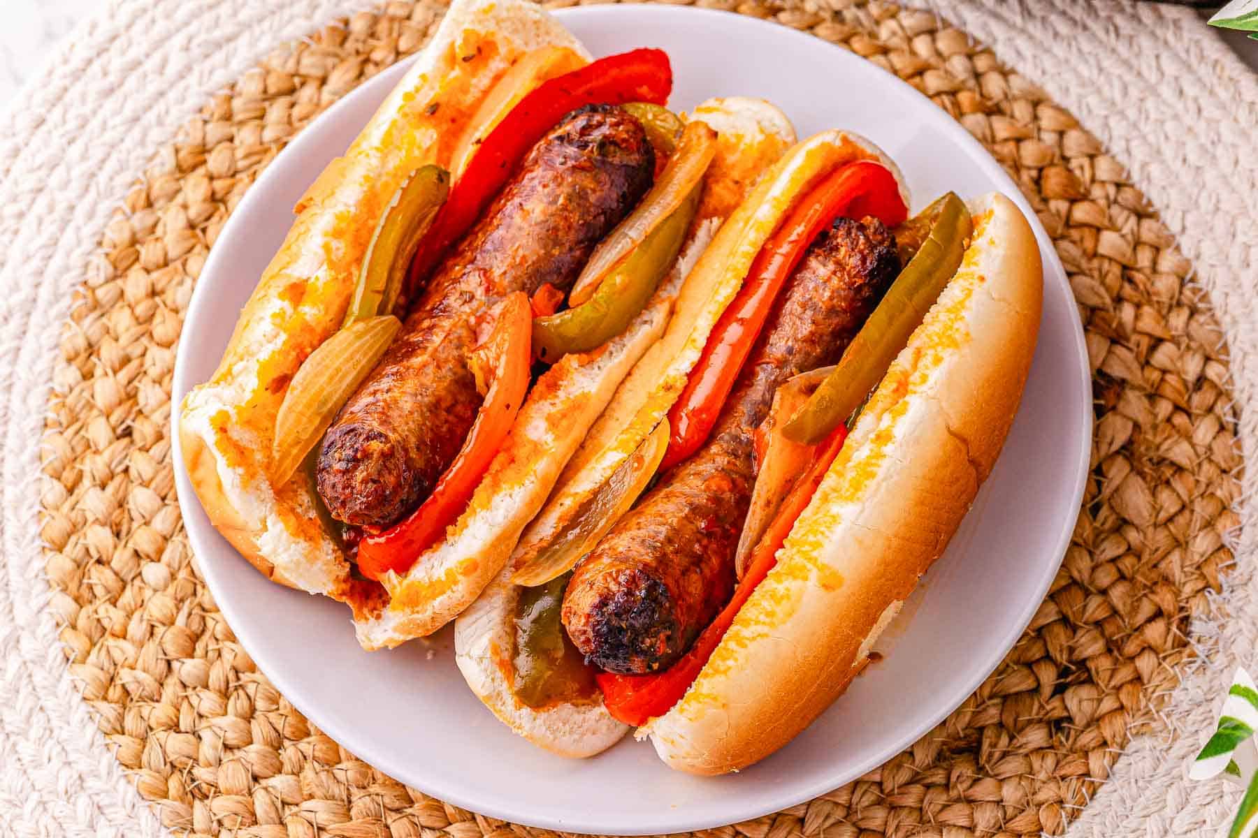 Two sausage and peppers sandwiches with grilled onions served on a white plate&mdash;a classic recipe perfect for fans of hearty Crockpot meals.