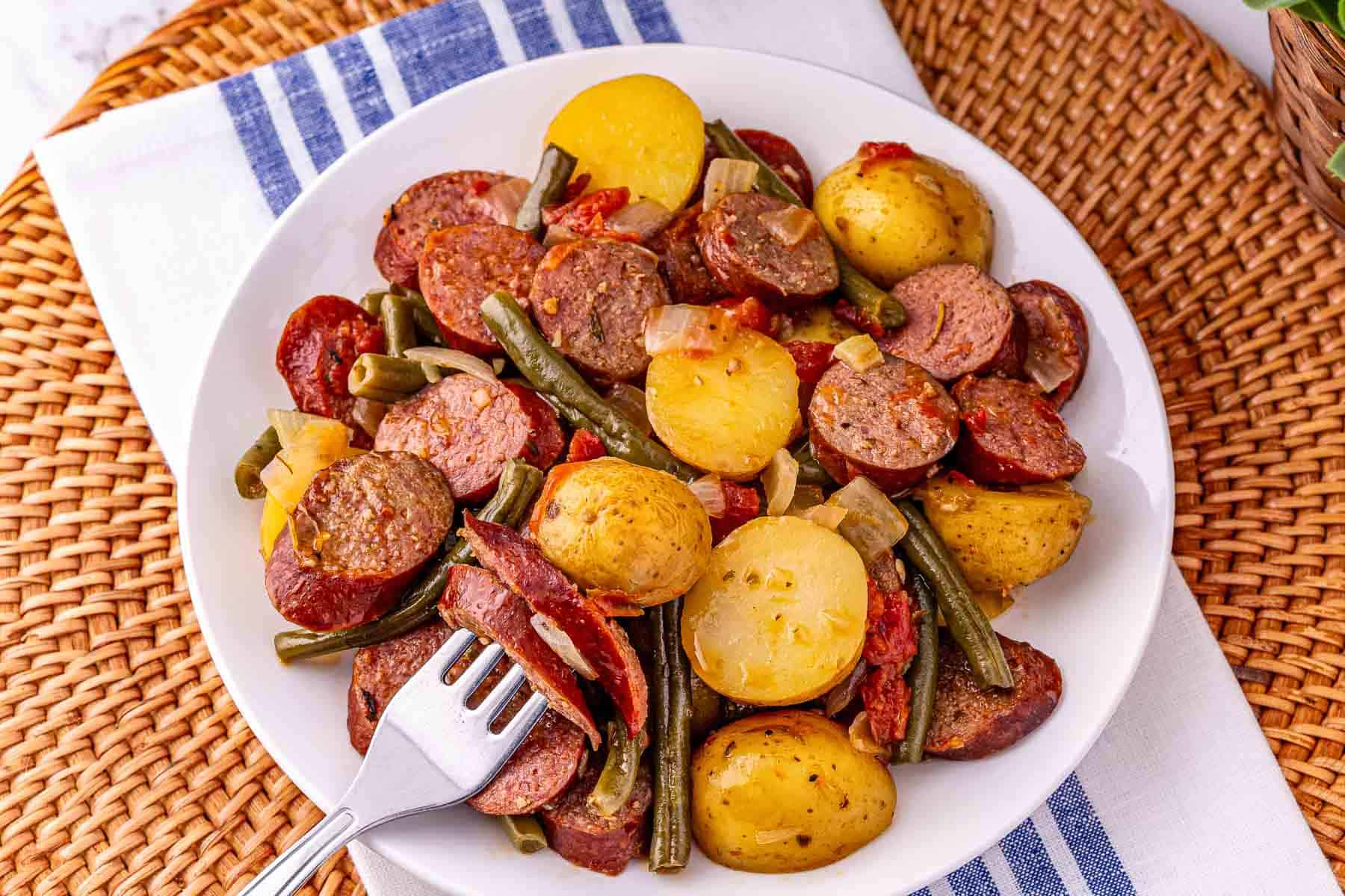 A plate of savory sausage and potatoes, green beans, and onions, with a fork resting on the food&mdash;classic comfort made easy, just like crockpot sausage dishes.