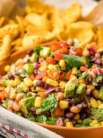 Colorful bean and corn salad in a bowl, surrounded by golden corn chips on a tray.