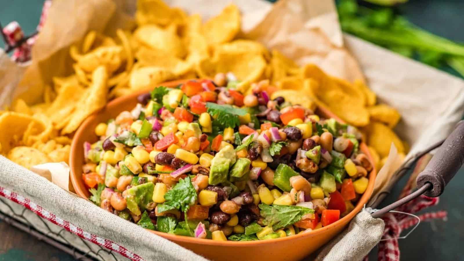 Colorful bean and corn salad in a bowl, surrounded by golden corn chips on a tray.