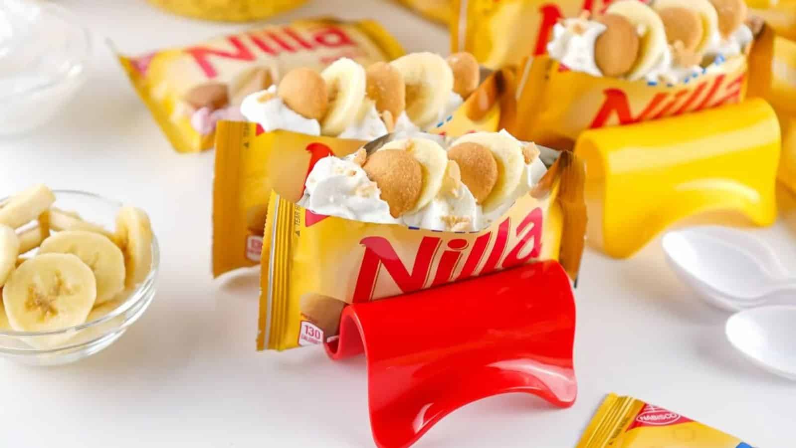 Nilla wafer packs filled with whipped cream, banana slices, and cookies, displayed with spoons and holders.