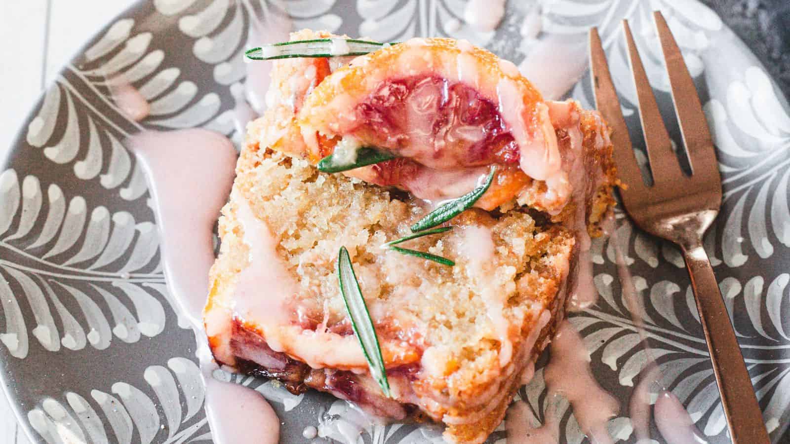 A slice of glazed cherry loaf cake garnished with rosemary on a patterned plate with a fork—perfect inspiration for simple cakes and easy cakes to enjoy at home.
