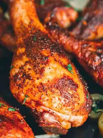 Close-up of seasoned, baked chicken drumsticks garnished with herbs, with sliced jalapeños nearby.