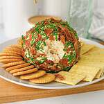 A ranch cheese ball coated with bacon and chives, served with round and square crackers on a white plate.