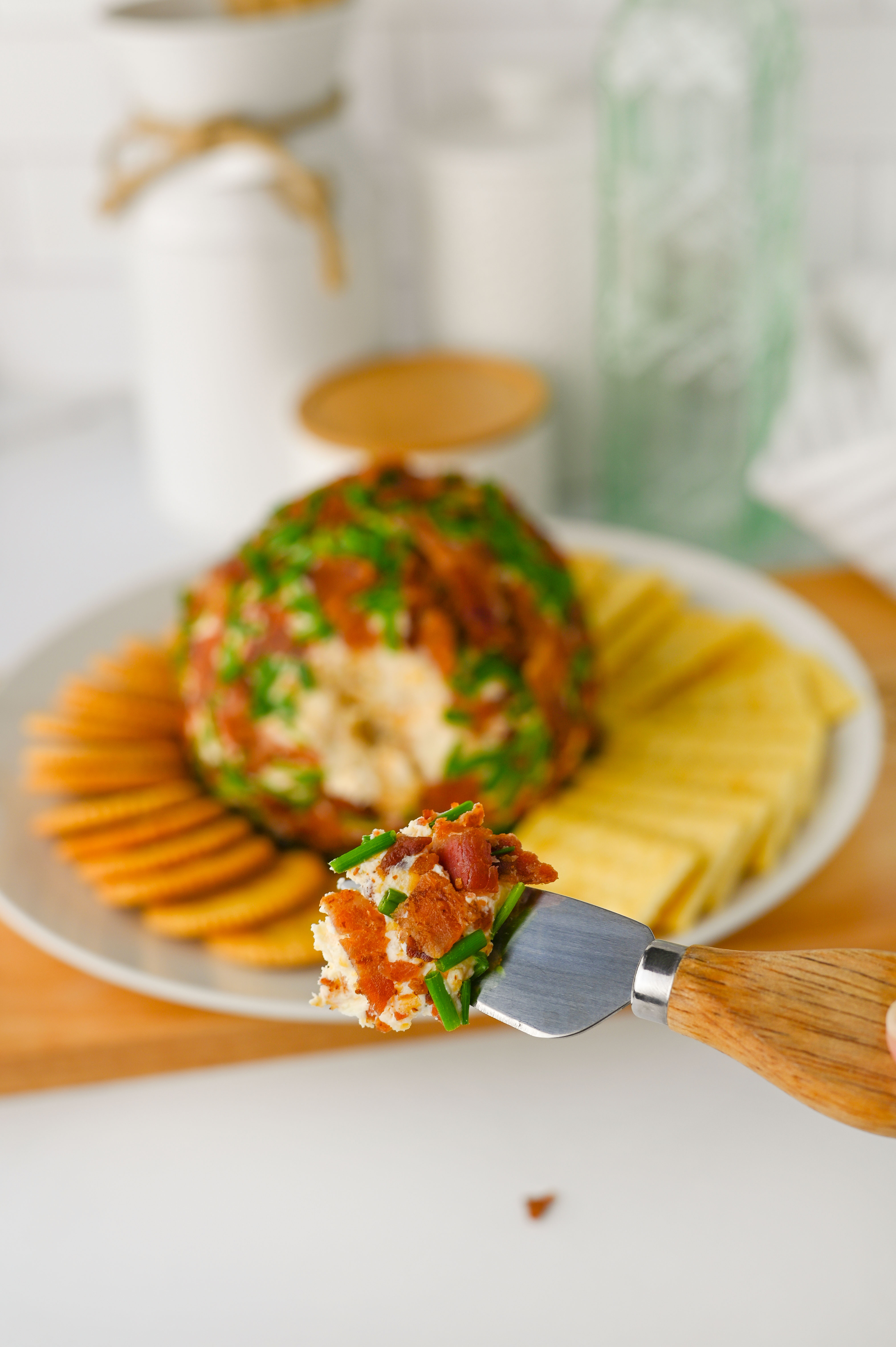 A fork holds a bite of cheesy bacon ball; ranch-flavored crackers and cheese balls are on a plate in the background.