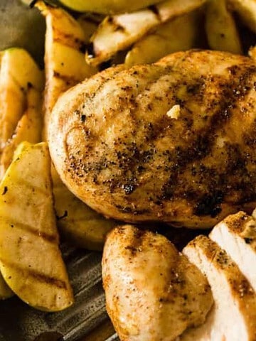 Grilled chicken breast with sliced pieces, roasted vegetables, and cornbread on a plate.