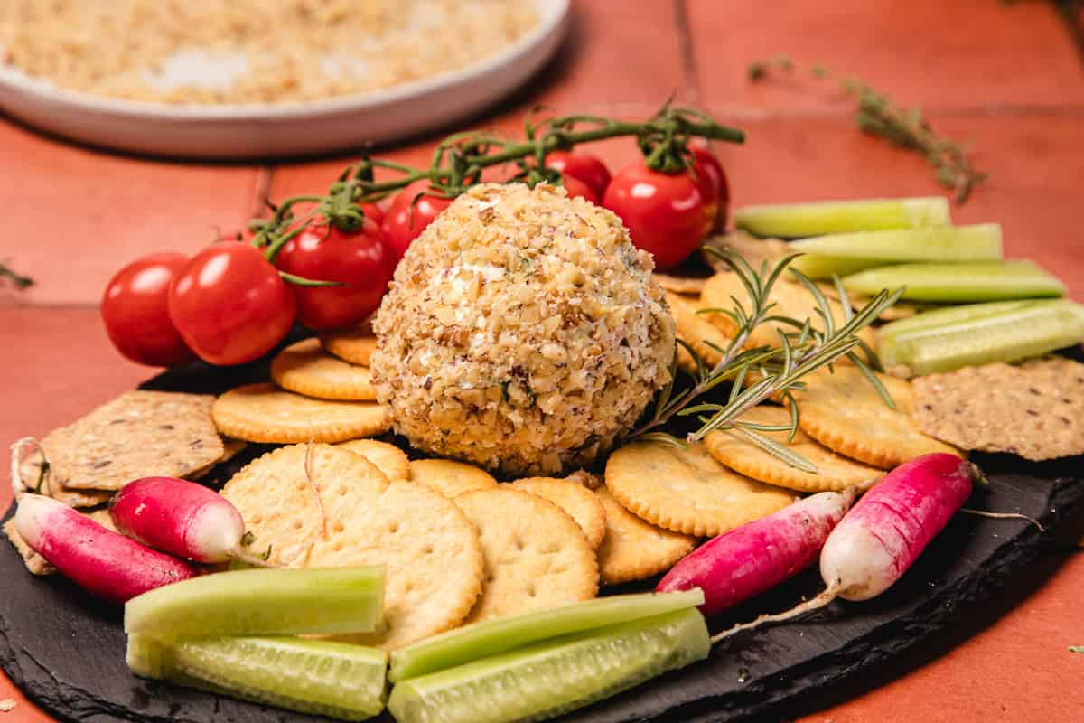 A southern cream cheese ball recipe with herbs, crackers, cherry tomatoes, radishes, and cucumber sticks arranged on a platter.
