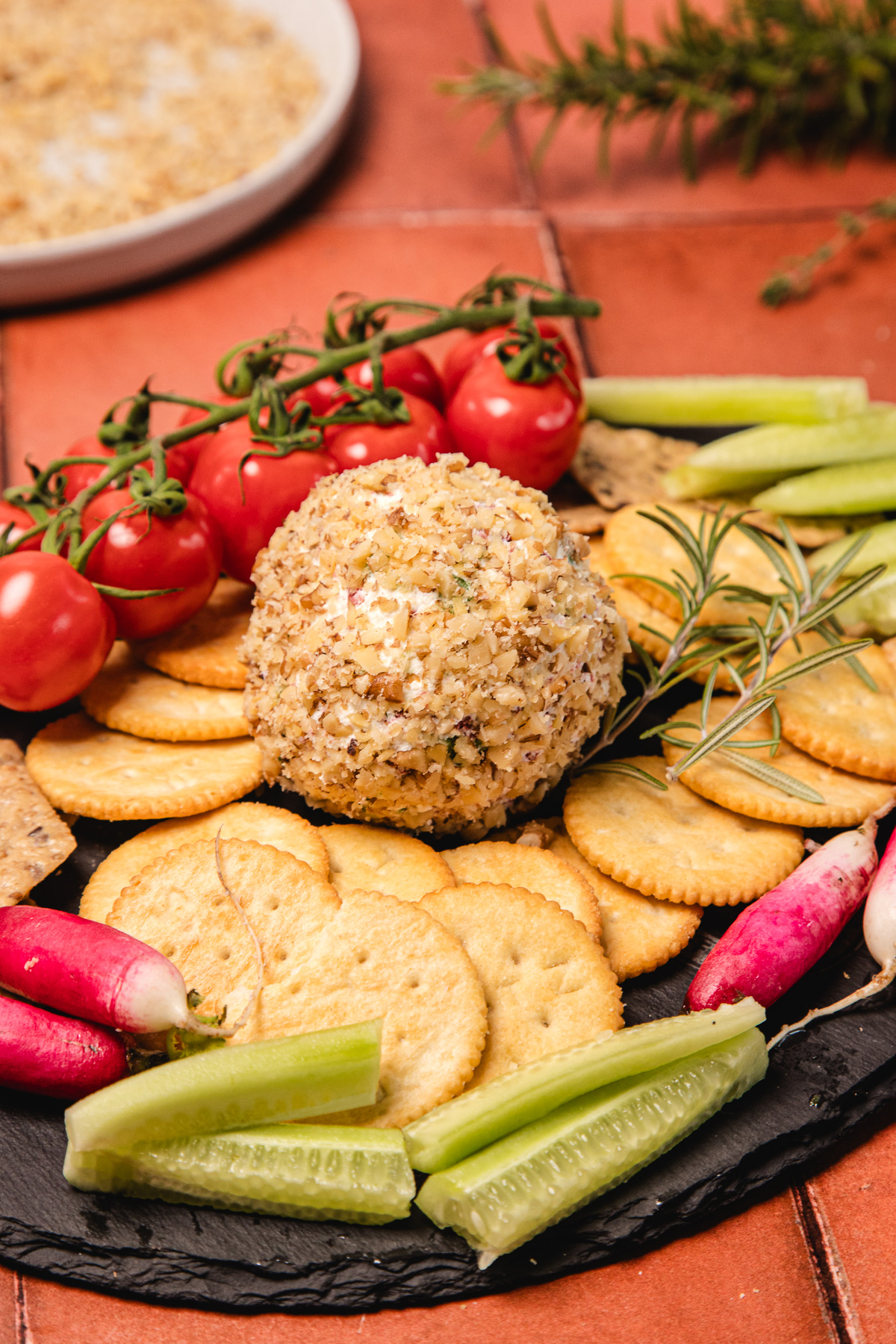 Cheese ball coated in nuts, inspired by a Southern cream cheese ball recipe, served with crackers, tomatoes, radishes, and cucumber slices on a platter.