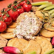 A southern cream cheese ball recipe served with crackers, cherry tomatoes, cucumber sticks, and radishes on a serving platter.