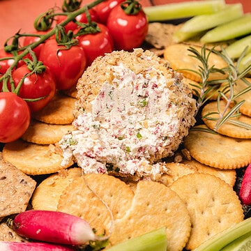 A southern cream cheese ball recipe served with crackers, cherry tomatoes, cucumber sticks, and radishes on a serving platter.