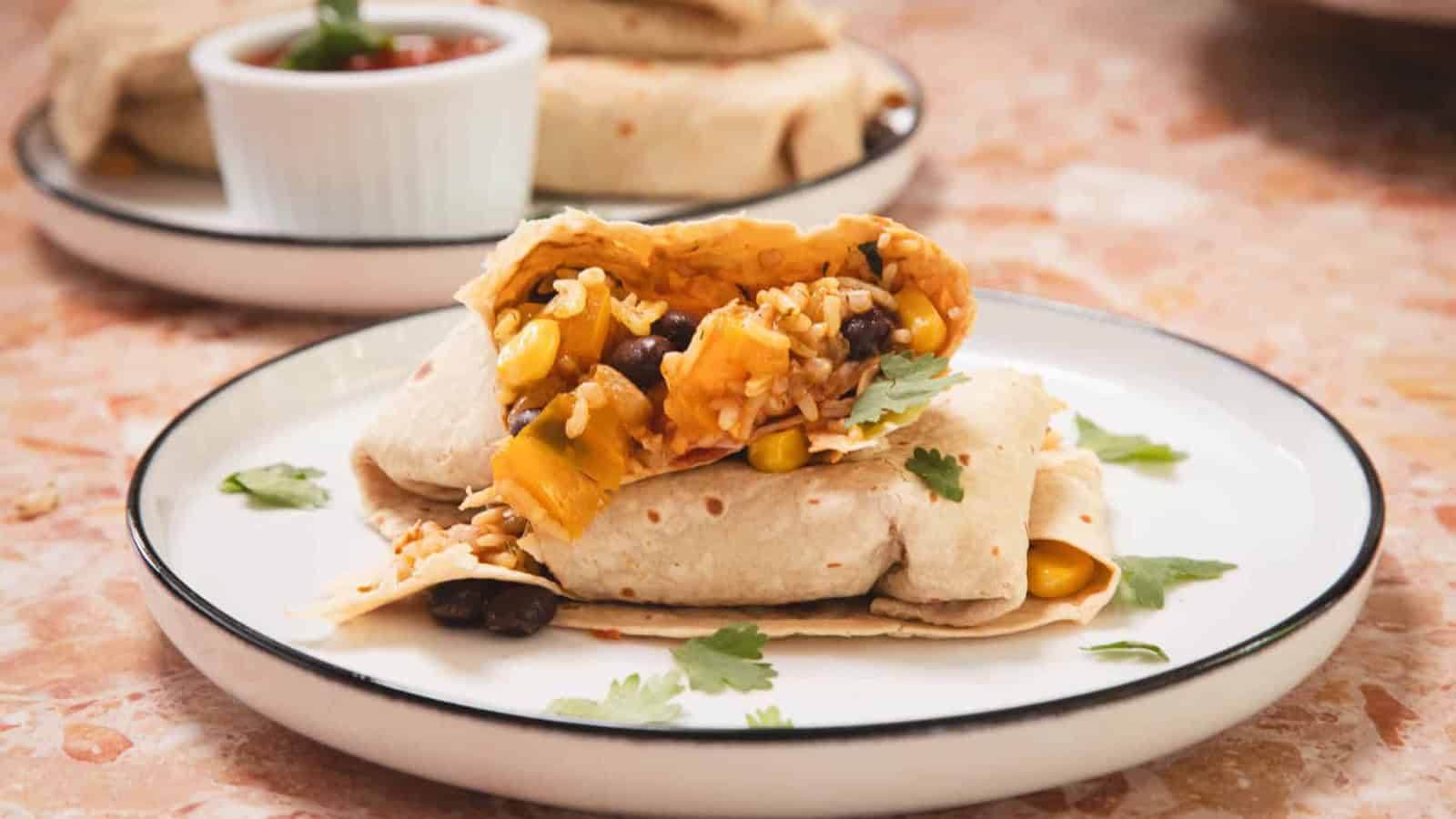 A burrito filled with rice, black beans, corn, and vegetables on a white plate, garnished with cilantro.