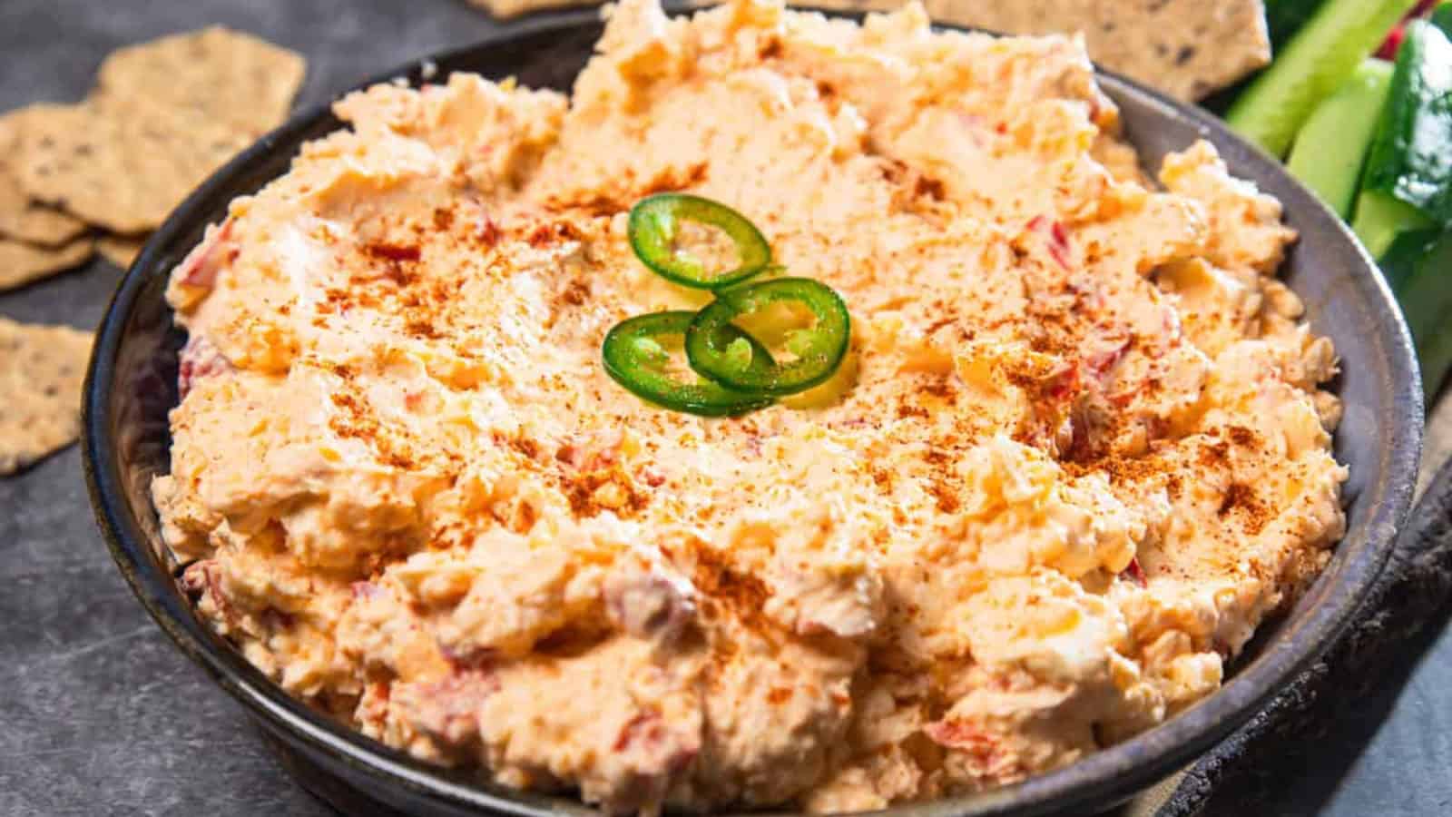 A bowl of creamy pimento cheese dip topped with sliced jalapeños and a sprinkle of paprika.