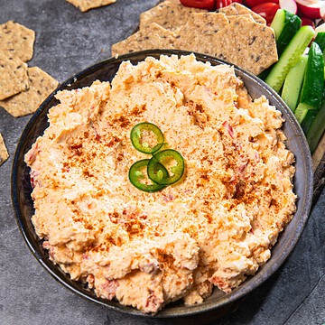 Creamy southern cheese dip topped with sliced jalapeños and paprika, served with crackers and fresh cucumber slices.