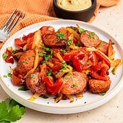 Air fryer kielbasa sausage slices with sautéed red peppers, onions, and parsley on a white plate, fork and dip nearby.