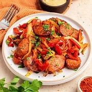 Sautéed air fryer kielbasa with onions and red peppers garnished with parsley, served with mustard on a white plate.