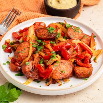 Air fryer kielbasa sausage slices with saut&eacute;ed red peppers, onions, and parsley on a white plate, fork and dip nearby.
