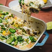 A cheesy huevos rancheros breakfast casserole topped with eggs, jalapeños, and herbs is being served from a blue baking dish.