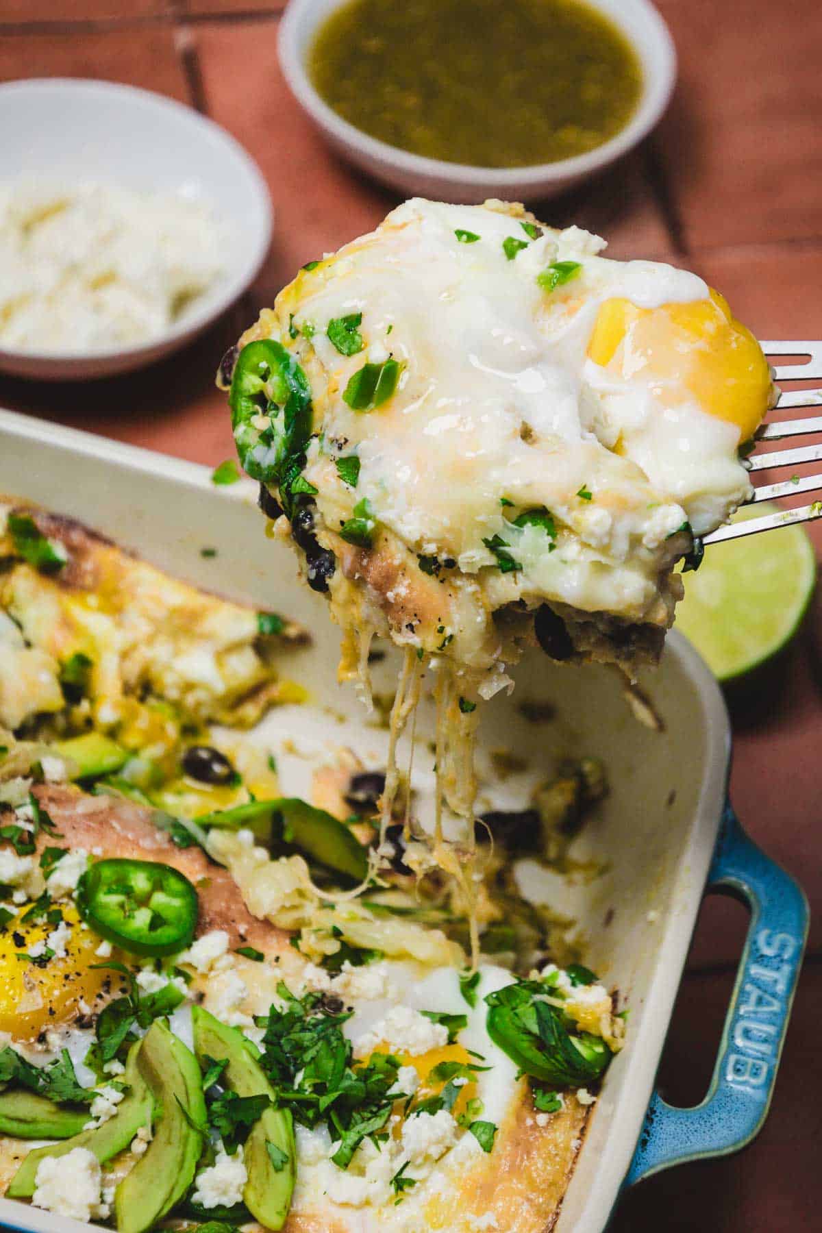 A cheesy baked dish with eggs, jalape&ntilde;os, and herbs being served from a blue casserole dish&mdash;this huevos rancheros breakfast casserole is perfect for kicking off your morning with a flavorful twist.