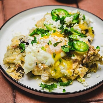 Eggs with crumbled cheese, jalape&ntilde;o slices, and herbs on a plate, yolk broken and running&mdash;reminiscent of the bold flavors found in a huevos rancheros breakfast casserole.
