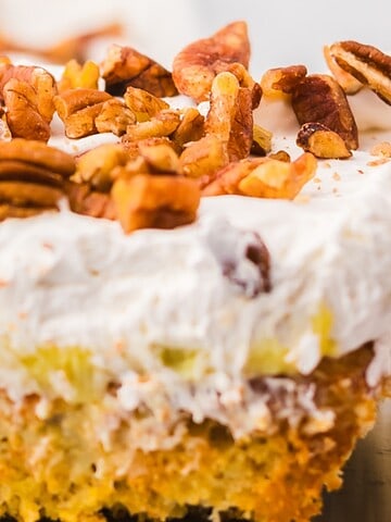 A slice of cake topped with whipped cream and chopped pecans on a metal spatula.