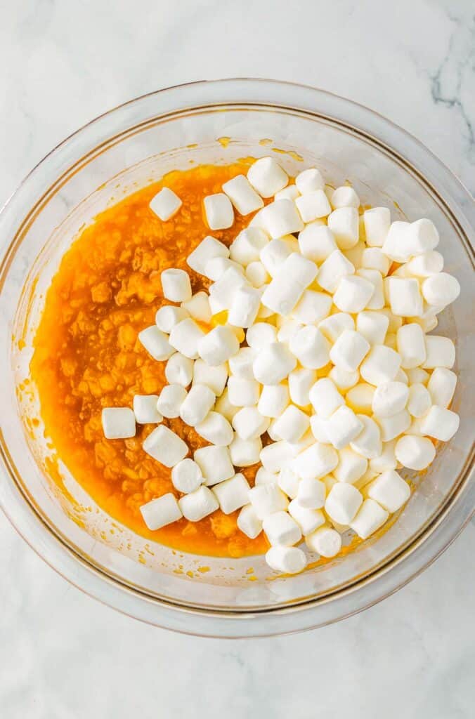 A glass bowl with mashed sweet potatoes and mini marshmallows sits on a marble surface, reminiscent of the cozy sweetness found in caramel apple fluff.