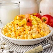 A bowl of creamy caramel apple fluff fruit salad with marshmallows, topped with fresh apple chunks, sits beside a glass of milk.