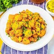 A white plate of seasoned potatoes garnished with herbs, inspired by Sheet Pan Mississippi Chicken and Potatoes, sits on a blue-striped cloth, with peppers on the side.