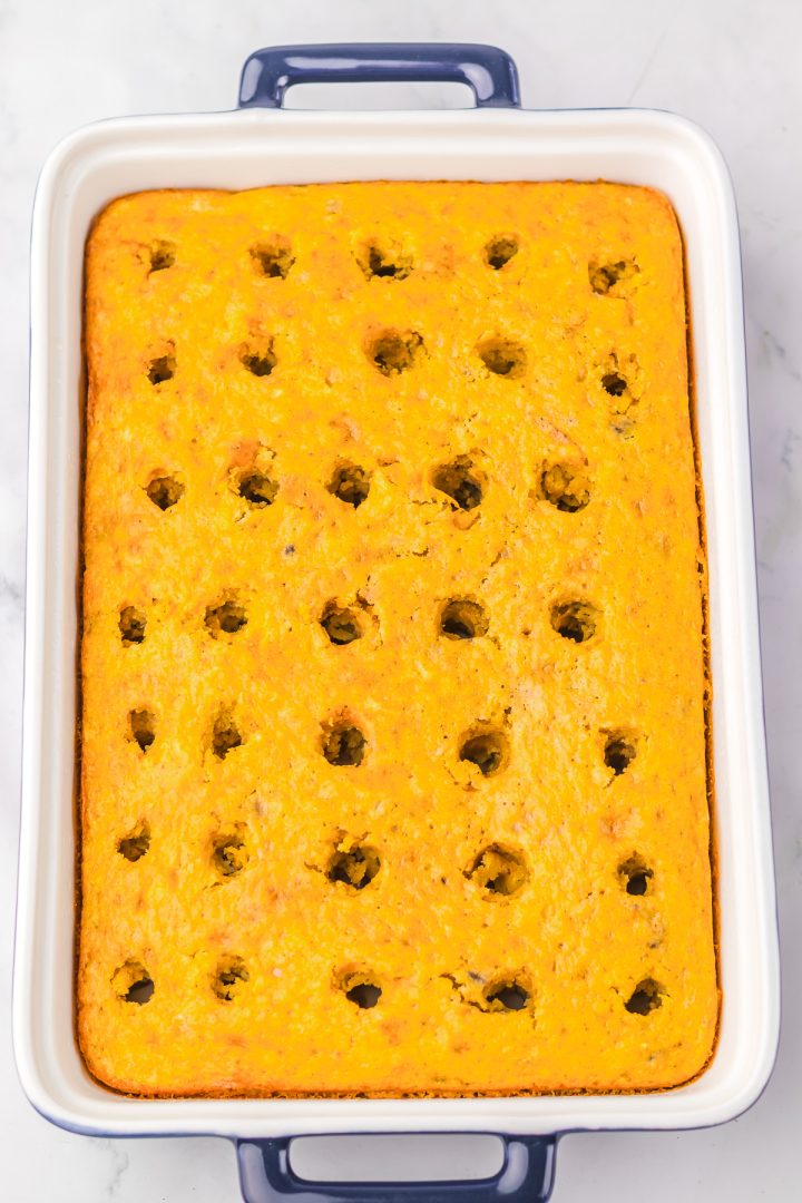 A rectangular Hummingbird Poke Cake with holes poked evenly across the top, in a white dish with blue handles.