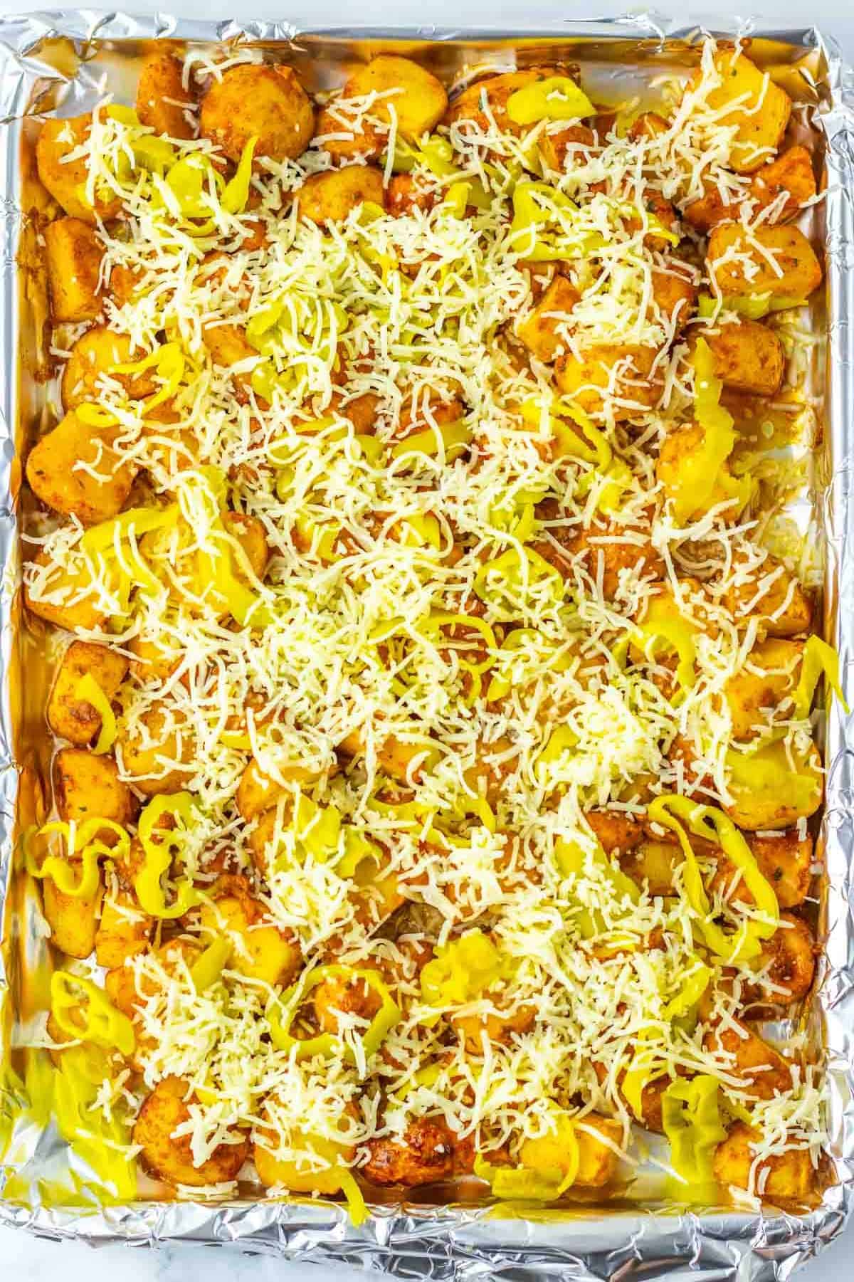 Sliced potatoes with cheese and pepper rings on a foil-lined baking sheet, reminiscent of Sheet Pan Mississippi Chicken and Potatoes, ready to be baked.