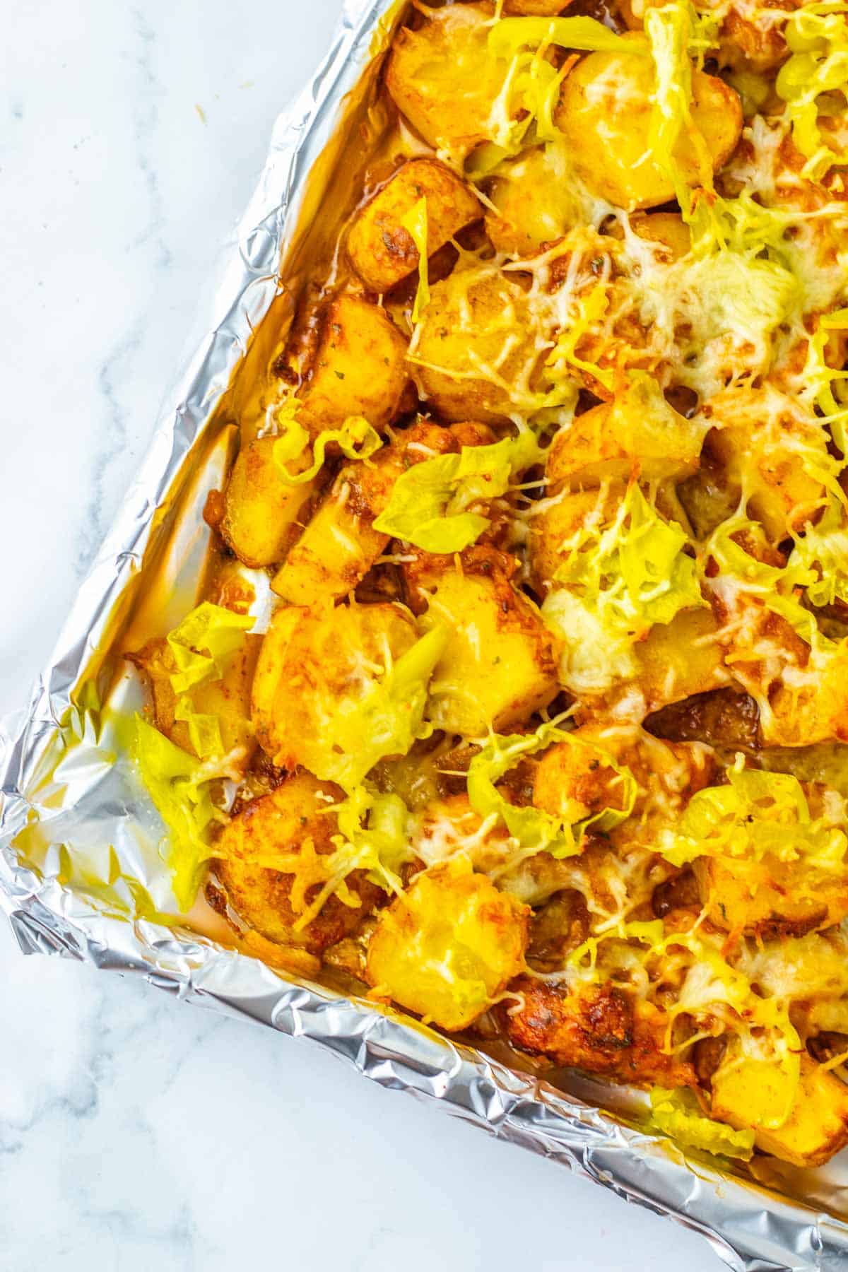 Sheet Pan Mississippi Chicken and Potatoes: Sliced roasted potatoes with melted cheese and pepperoncini on a foil-lined baking sheet, perfectly complementing tender, flavorful chicken for an easy, delicious all-in-one meal.
