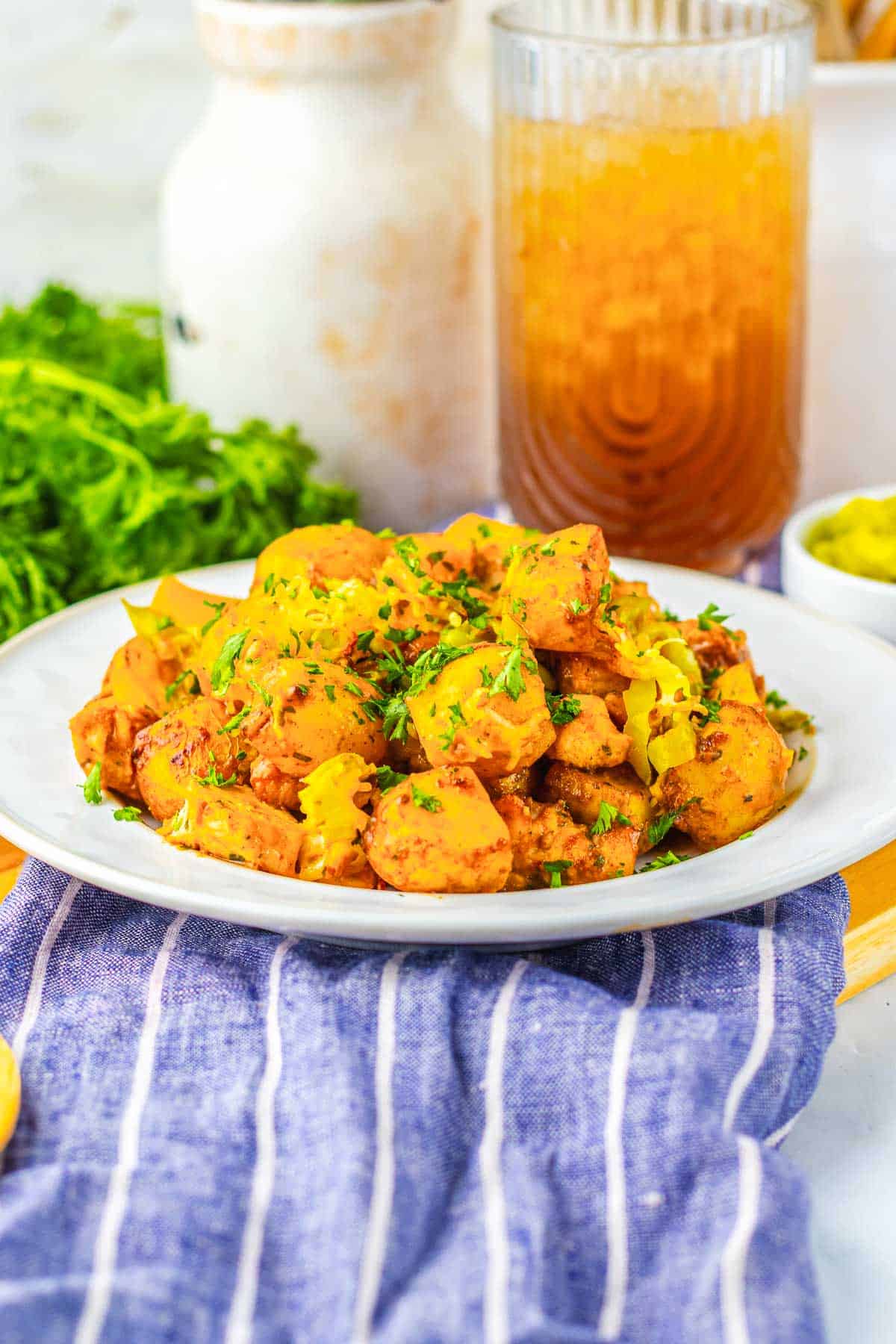 A plate of seasoned potatoes&mdash;reminiscent of Sheet Pan Mississippi Chicken and Potatoes&mdash;garnished with herbs sits on a table, accompanied by a refreshing drink and fresh greens in the background.