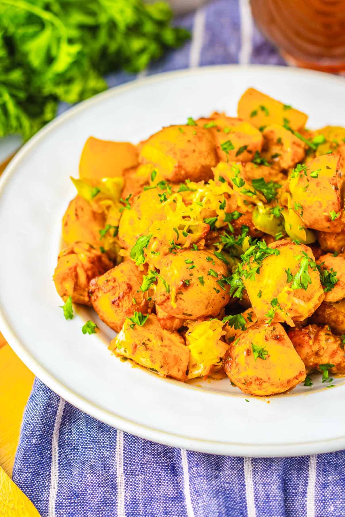 A white plate of spicy cooked potatoes, inspired by Sheet Pan Mississippi Chicken and Potatoes, garnished with chopped herbs, on a blue-striped cloth.