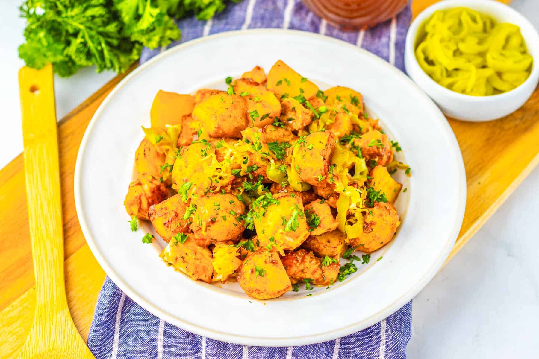 A plate of roasted potatoes with herbs and cheese, reminiscent of Sheet Pan Mississippi Chicken and Potatoes, served on a white dish next to a bowl of sliced peppers.