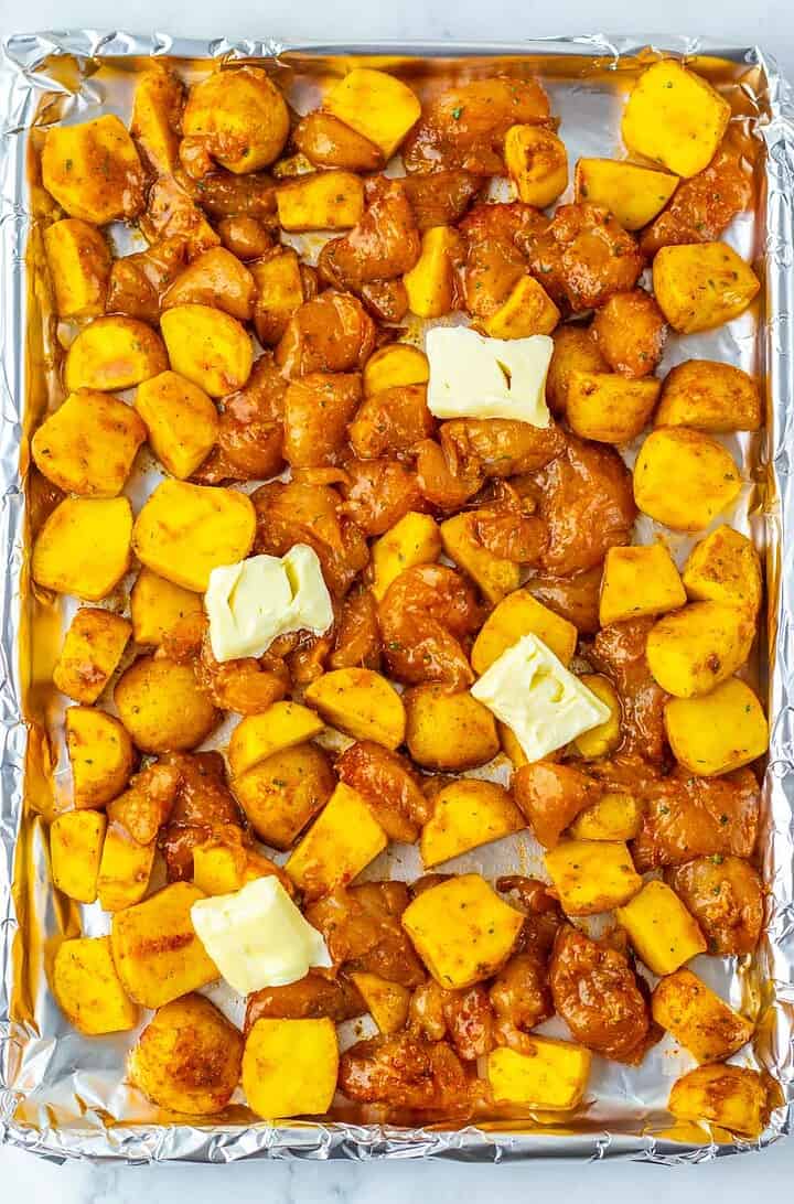 Sheet Pan Mississippi Chicken and Potatoes features diced potatoes and seasoned chicken with butter pats on a foil-lined baking sheet, ready to be cooked.