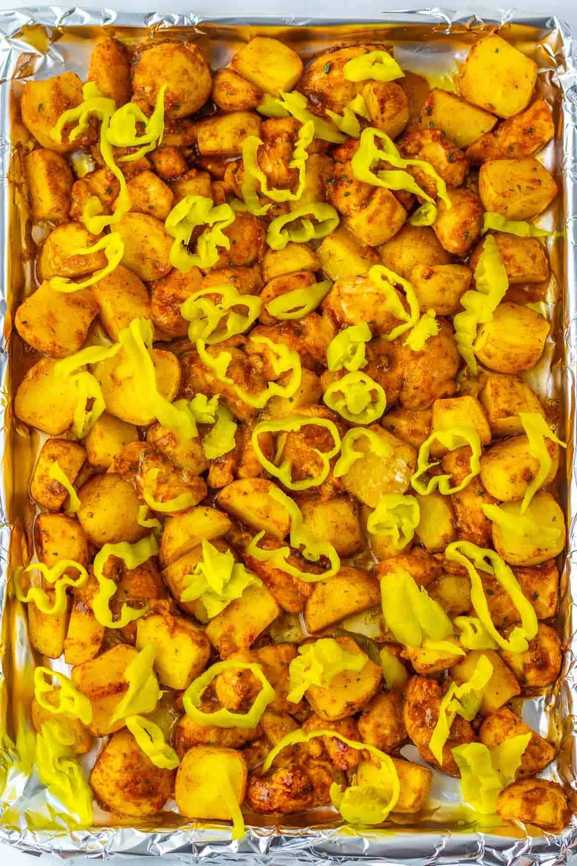 Roasted potato chunks on a foil-lined baking sheet, topped with sliced yellow pickled peppers&mdash;just like the flavorful sides in a Sheet Pan Mississippi Chicken and Potatoes dinner.